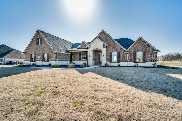 french country style house with stone siding, brick siding, and a front yard