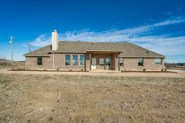 back of house with a patio area, brick siding, a chimney, and roof with shingles