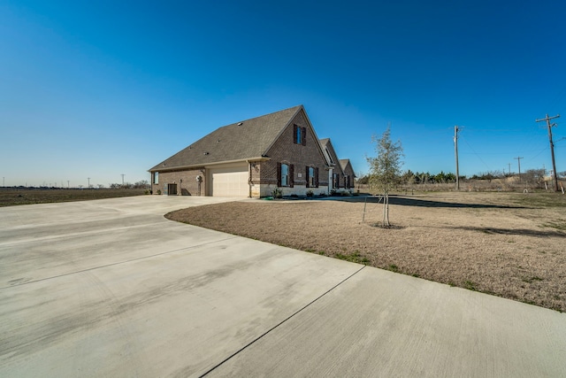 view of side of home featuring driveway, an attached garage, and brick siding