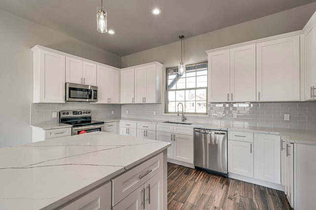 kitchen with stainless steel appliances, white cabinetry, a sink, and light stone counters