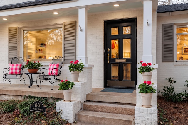 entrance to property featuring a porch, brick siding, and a shingled roof