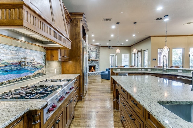 kitchen with brown cabinets, custom range hood, stainless steel gas stovetop, and visible vents