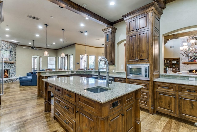 kitchen with a fireplace, a sink, open floor plan, light wood-type flooring, and stainless steel microwave