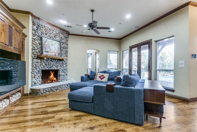 living room with arched walkways, crown molding, visible vents, a stone fireplace, and wood finished floors