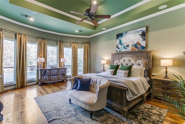 bedroom with visible vents, a raised ceiling, wood finished floors, and ornamental molding