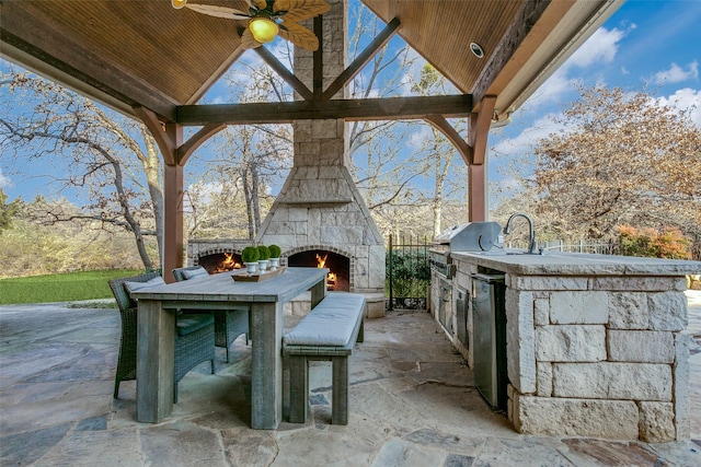 view of patio / terrace featuring ceiling fan, exterior kitchen, and an outdoor stone fireplace