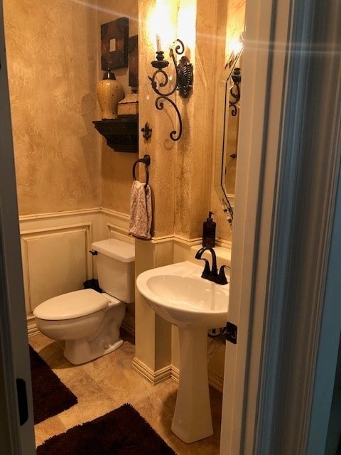 bathroom with toilet, a wainscoted wall, a decorative wall, and a sink