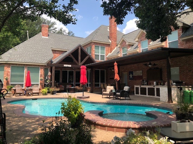 back of house featuring a patio area, a pool with connected hot tub, a chimney, and brick siding