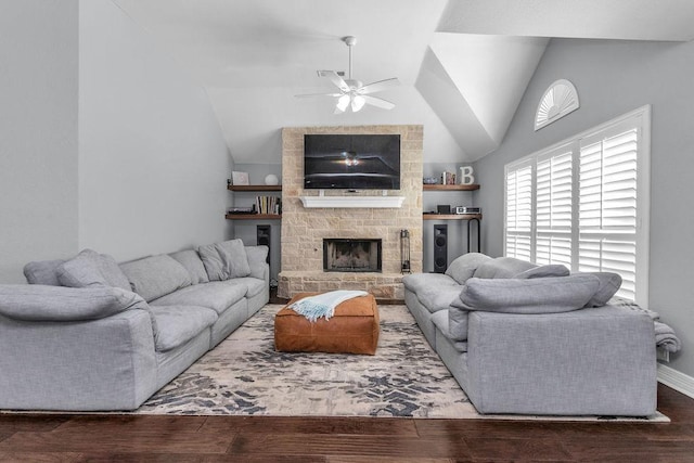 living room with lofted ceiling, a ceiling fan, a stone fireplace, wood finished floors, and baseboards