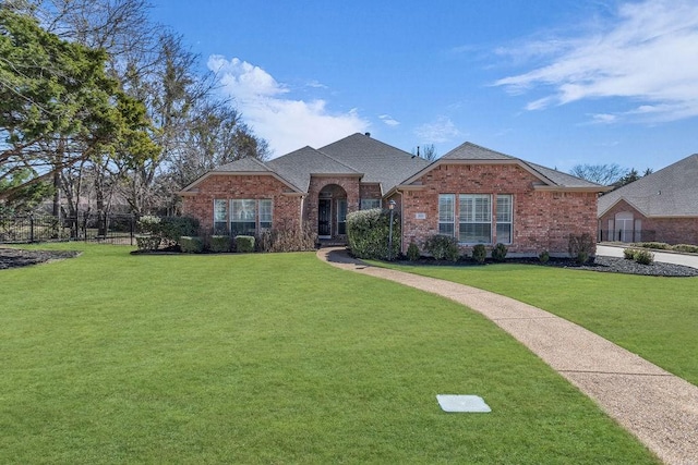 view of front of home featuring a shingled roof, a front yard, fence, and brick siding