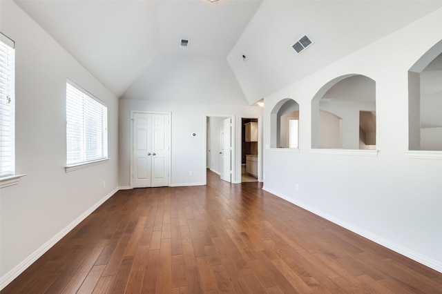 empty room featuring high vaulted ceiling, dark wood-type flooring, visible vents, and baseboards