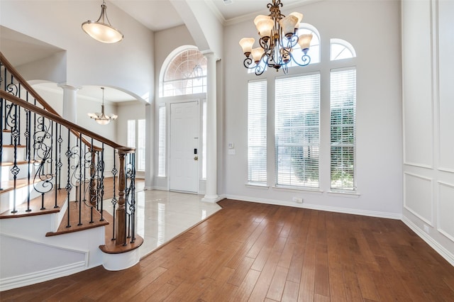 entrance foyer featuring a notable chandelier, crown molding, wood finished floors, stairway, and ornate columns