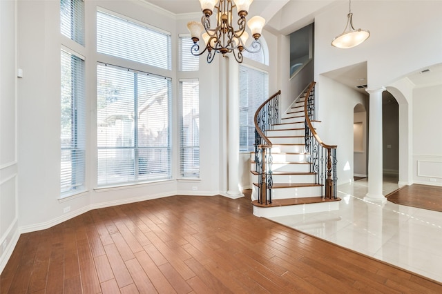 foyer entrance featuring arched walkways, crown molding, a high ceiling, wood finished floors, and stairs