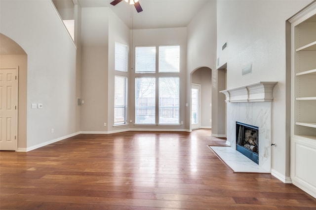 unfurnished living room with arched walkways, hardwood / wood-style flooring, ceiling fan, a high ceiling, and a high end fireplace