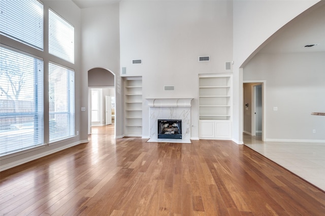 unfurnished living room with arched walkways, a premium fireplace, light wood-type flooring, and visible vents