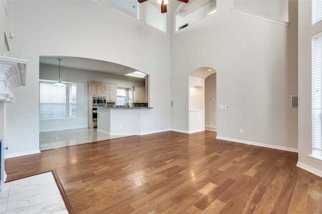 unfurnished living room featuring arched walkways, ceiling fan, baseboards, and light wood-style floors