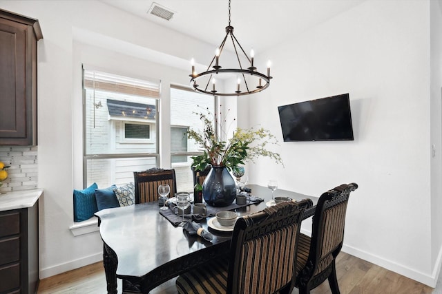 dining room with light wood finished floors, an inviting chandelier, visible vents, and baseboards