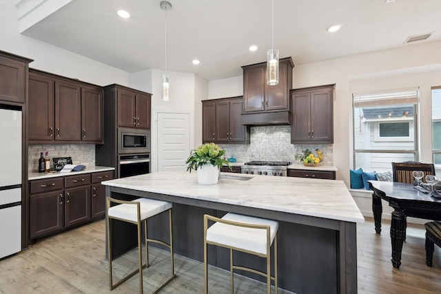 kitchen featuring appliances with stainless steel finishes, light wood-style floors, dark brown cabinetry, and a breakfast bar