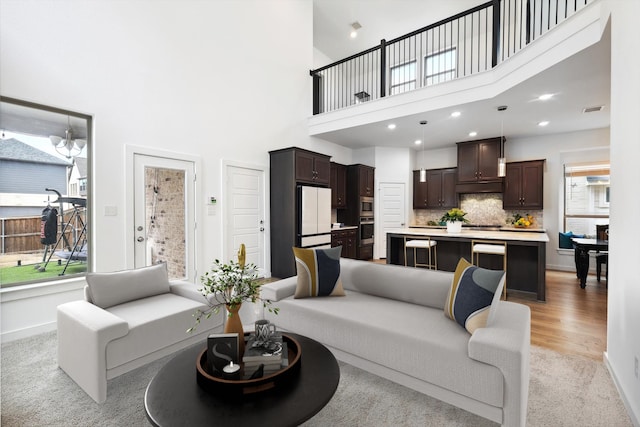 living area featuring visible vents, baseboards, a towering ceiling, light wood-type flooring, and recessed lighting