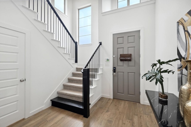 entrance foyer with stairs, baseboards, a towering ceiling, and light wood-style floors