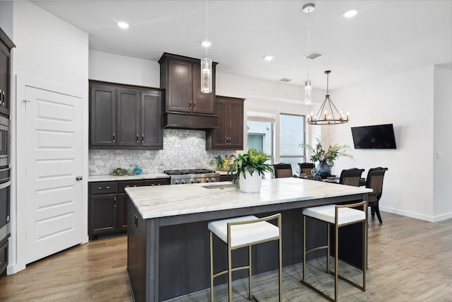 kitchen featuring a center island with sink, a breakfast bar area, hanging light fixtures, light wood-style flooring, and backsplash