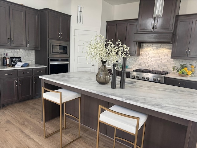 kitchen featuring tasteful backsplash, stainless steel appliances, light wood-style floors, and a kitchen breakfast bar