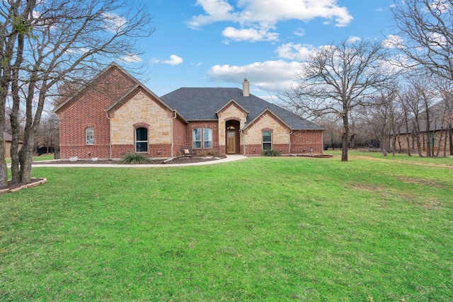 french country inspired facade with brick siding, roof with shingles, a chimney, stone siding, and a front lawn