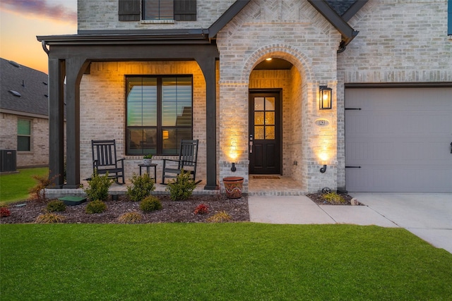 doorway to property featuring covered porch, brick siding, a lawn, and an attached garage