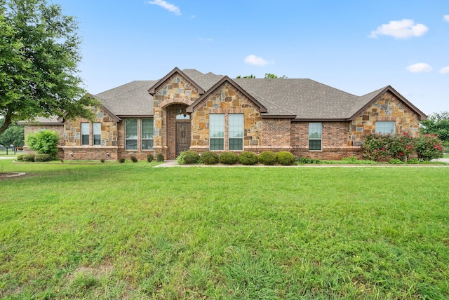 view of front of home with stone siding, a front lawn, a shingled roof, and brick siding