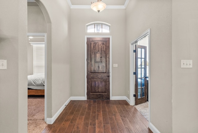 foyer entrance featuring arched walkways, crown molding, baseboards, and wood finished floors