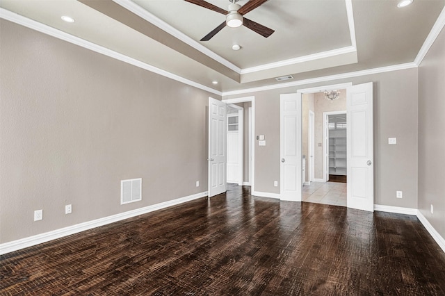 unfurnished bedroom featuring baseboards, visible vents, ornamental molding, wood finished floors, and a tray ceiling