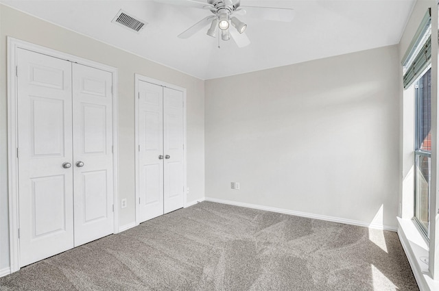 unfurnished bedroom with baseboards, visible vents, a ceiling fan, carpet flooring, and multiple closets