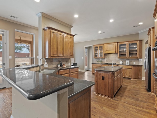 kitchen featuring a kitchen island with sink, visible vents, a sink, and a peninsula