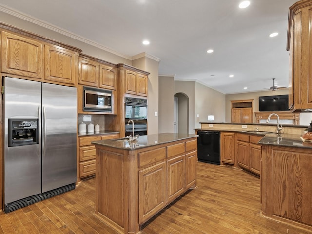 kitchen with light wood-style floors, arched walkways, a sink, and black appliances