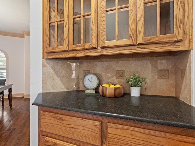 kitchen featuring arched walkways, ornamental molding, backsplash, dark wood-style floors, and brown cabinetry