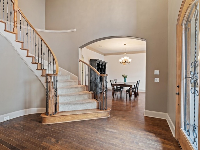 foyer entrance featuring baseboards, arched walkways, hardwood / wood-style floors, a high ceiling, and stairs