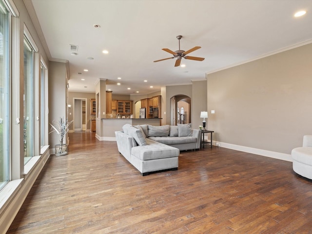 living room with baseboards, crown molding, arched walkways, and wood finished floors