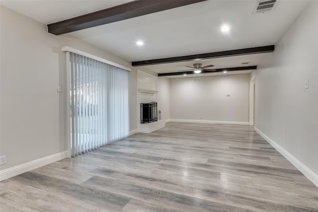 unfurnished living room with visible vents, baseboards, a brick fireplace, beam ceiling, and light wood finished floors