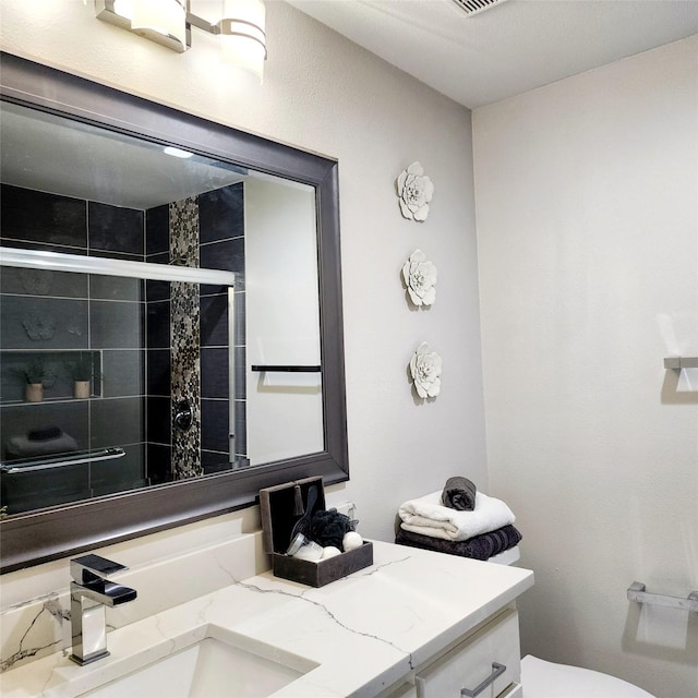 bathroom with visible vents, a tile shower, vanity, and toilet