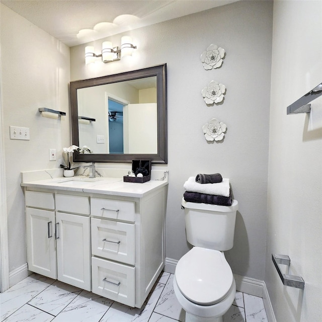 half bathroom with marble finish floor, toilet, vanity, and baseboards