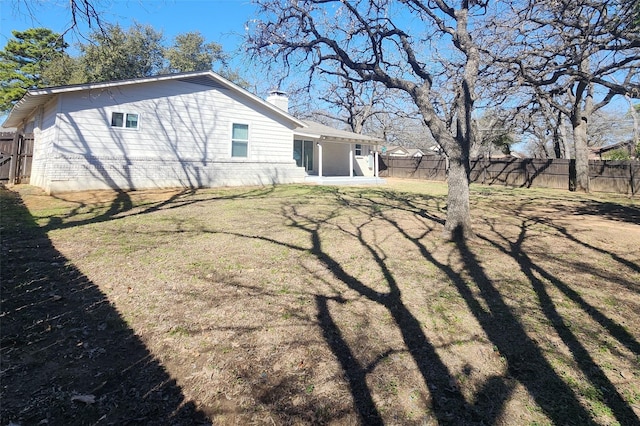 rear view of house with a sunroom, a fenced backyard, a yard, and a chimney