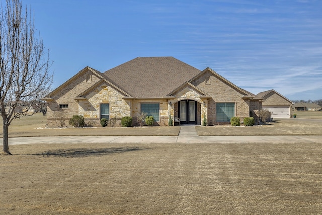 french country inspired facade featuring stone siding, roof with shingles, and brick siding