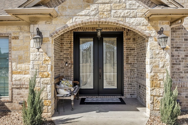 entrance to property with stone siding, french doors, and brick siding