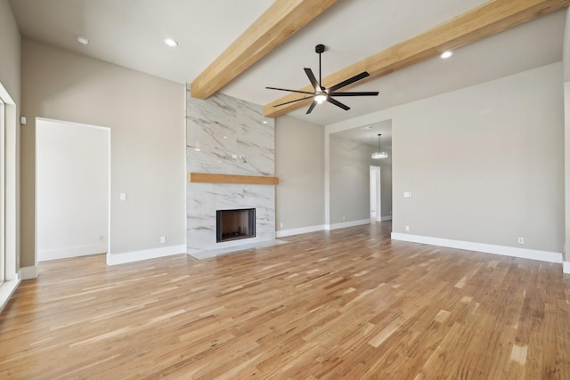 unfurnished living room with a premium fireplace, a ceiling fan, baseboards, light wood-type flooring, and beam ceiling