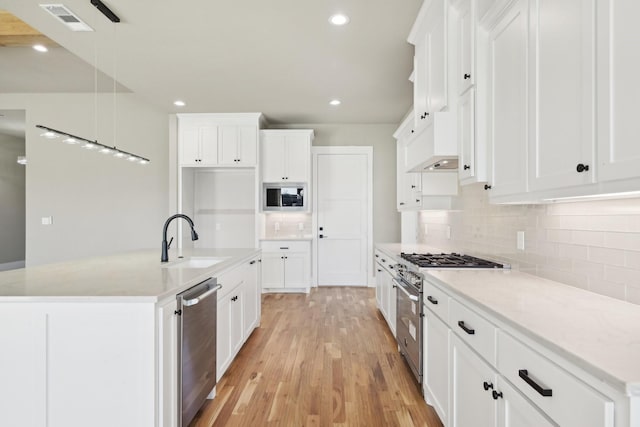 kitchen with decorative backsplash, white cabinets, appliances with stainless steel finishes, light wood-type flooring, and a sink