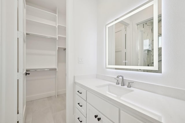 bathroom with a walk in closet, vanity, and baseboards