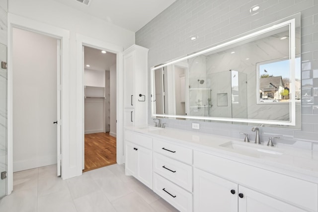 full bath featuring double vanity, a marble finish shower, a walk in closet, and a sink