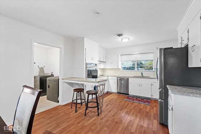 kitchen featuring appliances with stainless steel finishes, white cabinets, washer and dryer, and ornamental molding