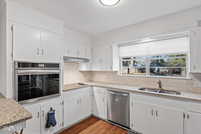 kitchen featuring crown molding, stainless steel appliances, decorative backsplash, a sink, and under cabinet range hood