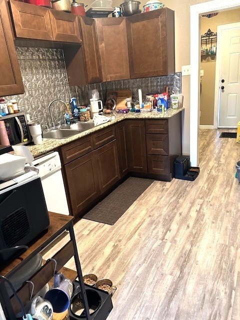 kitchen with tasteful backsplash, stainless steel microwave, light wood-style flooring, a sink, and dishwasher